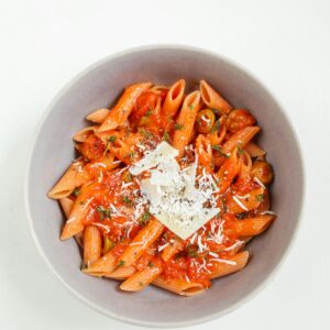 Top view of a white bowl filled with penne pasta in red sauce and cheese. Perfect for food photography.