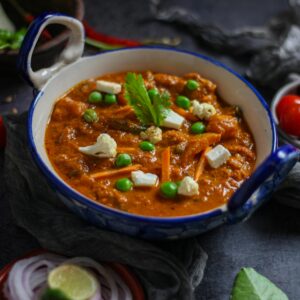 LA BELA FOODS - BARAMA Close-up of vibrant Indian mattar paneer curry with fresh ingredients in a ceramic bowl.