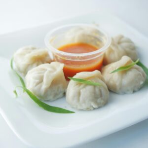 LA BELA FOODS - BARAMA A close-up of delicious steamed dumplings served with spicy sauce on a white plate.