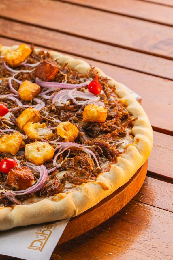 Close-up of a savory BBQ pulled pork pizza, garnished with red onions, croutons, and cherry tomatoes on a wooden board.